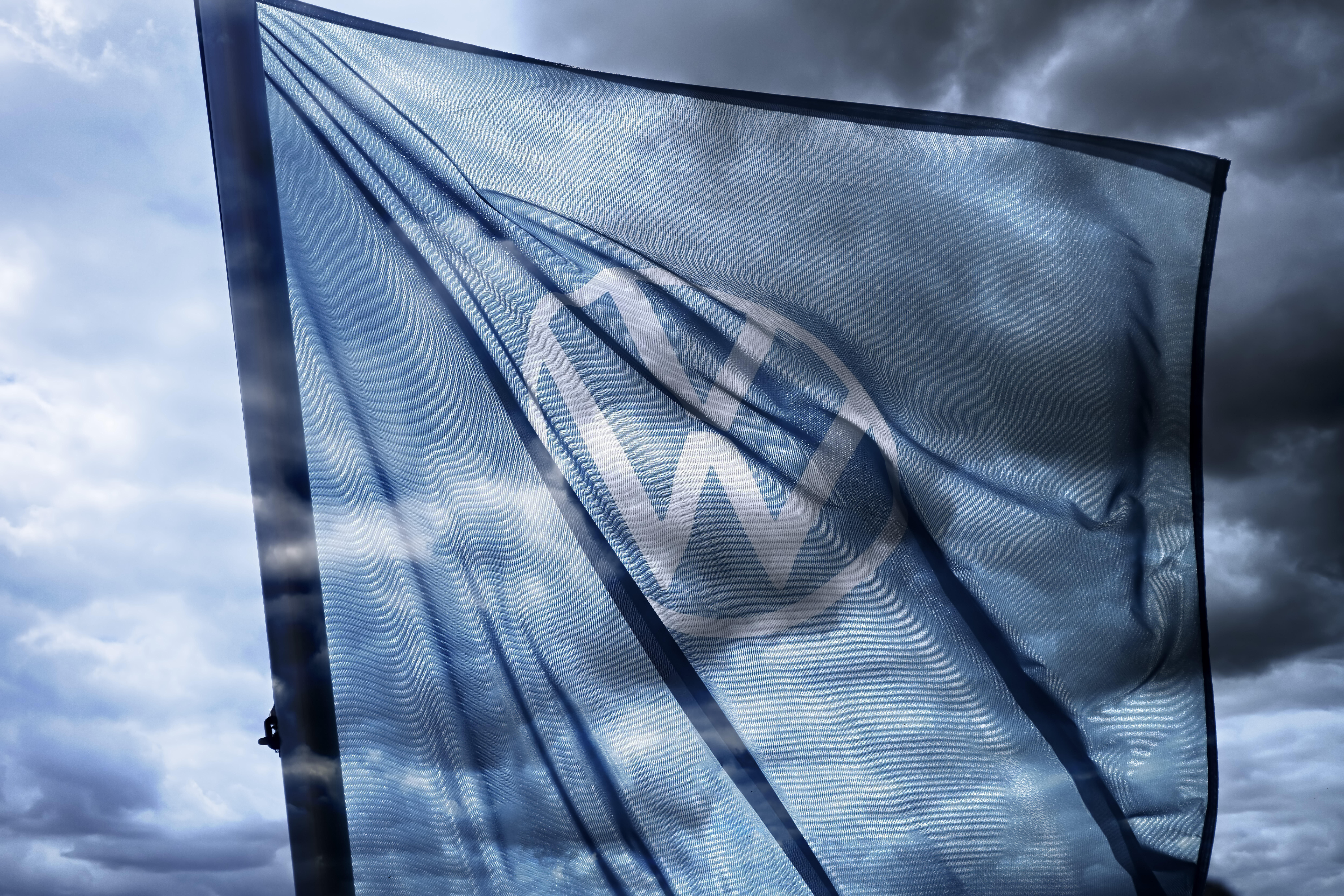 VW-Zeichen auf der Fahne eines Autohändlers, die vor dunklem Himmel weht.