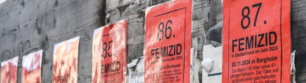 Rote Plakate mit Informationen über Femizide an einem Bauzaun