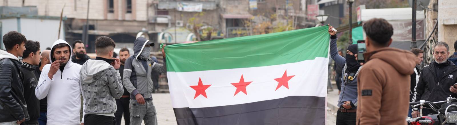 Junge Männer laufen mit aufgespannter syrischer Flagge durch die Stadt Hama