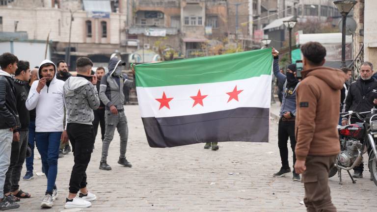 Junge Männer laufen mit aufgespannter syrischer Flagge durch die Stadt Hama