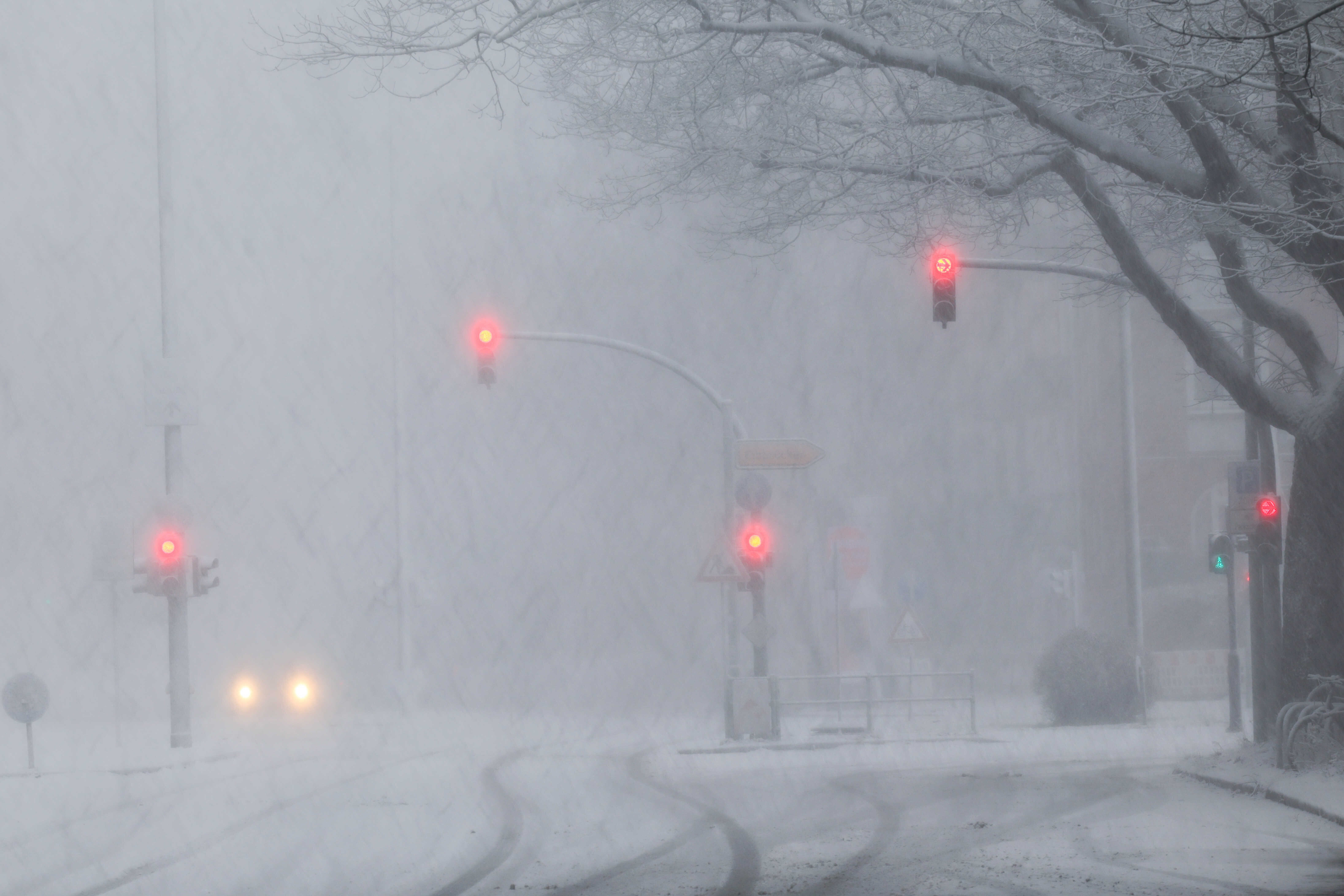 Scheinwerfer eines Autos und rot leuchtende Ampeln sind auf einer schneebedeckten Verkehrsstraße