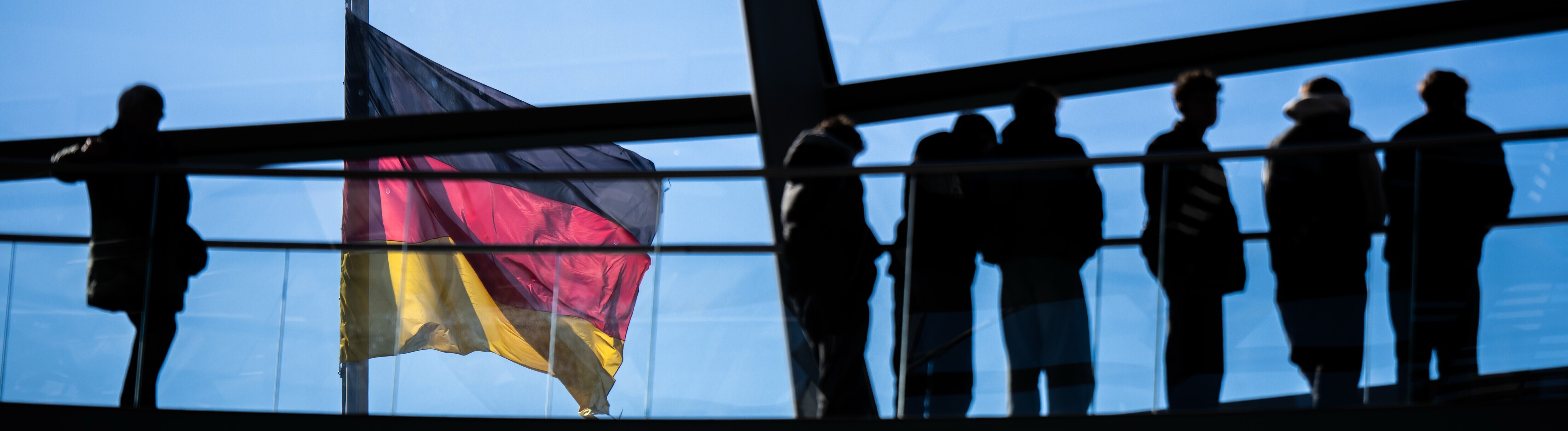 Besucher gehen vor der Deutschlandflagge in der Kuppel im Bundestag.