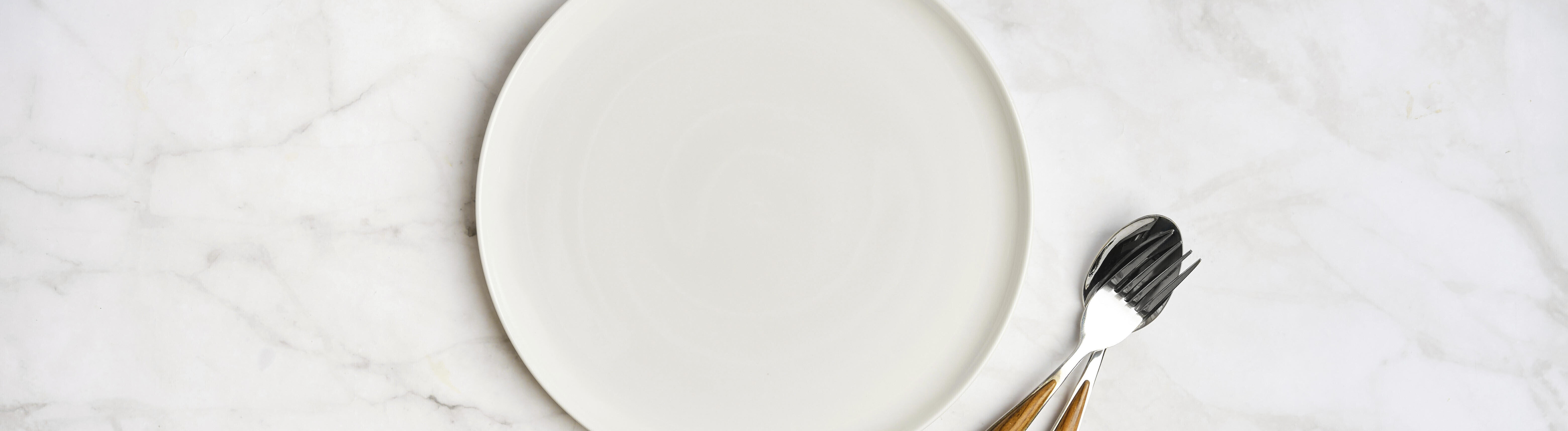 Ein leerer weißen Teller mit einer Gabel und einem Messer auf einer hellen Marmorfläche