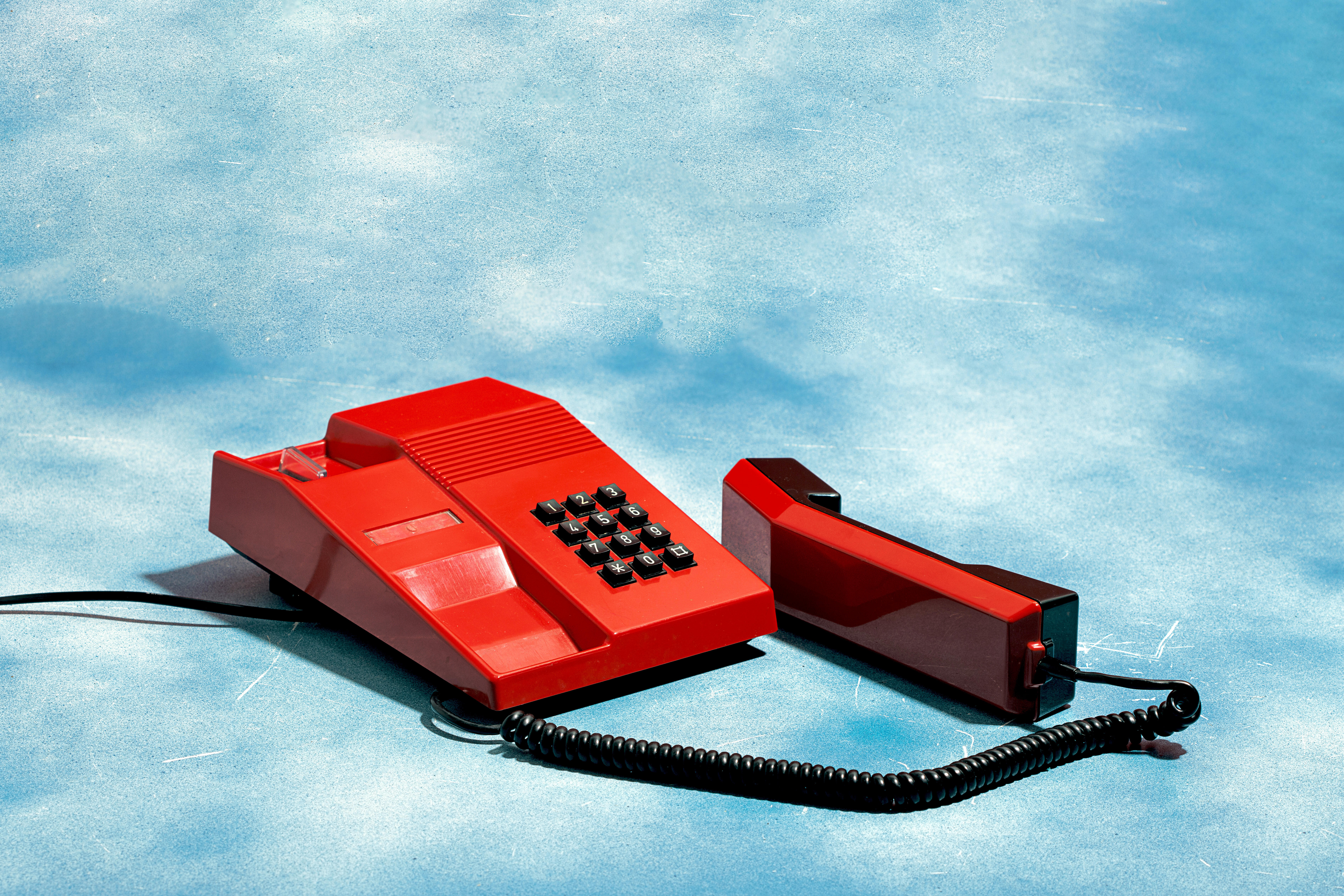 Ein rotes altes Telefon vor einem blau-weißen Hintergrund, der wie ein Wolkenhimmel aussieht
