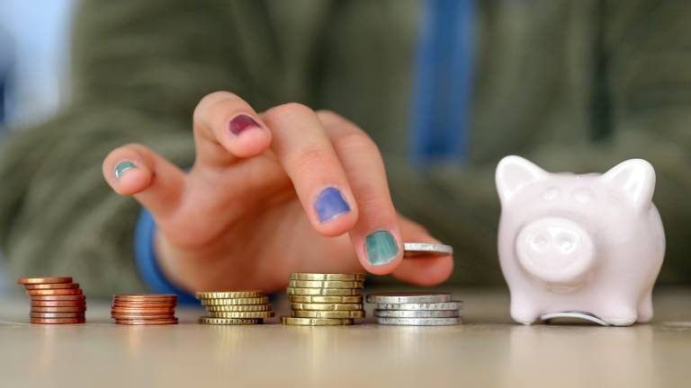 Hand mit lackierten Fingernägeln stapelt Geldmünzen neben einem Sparschwein