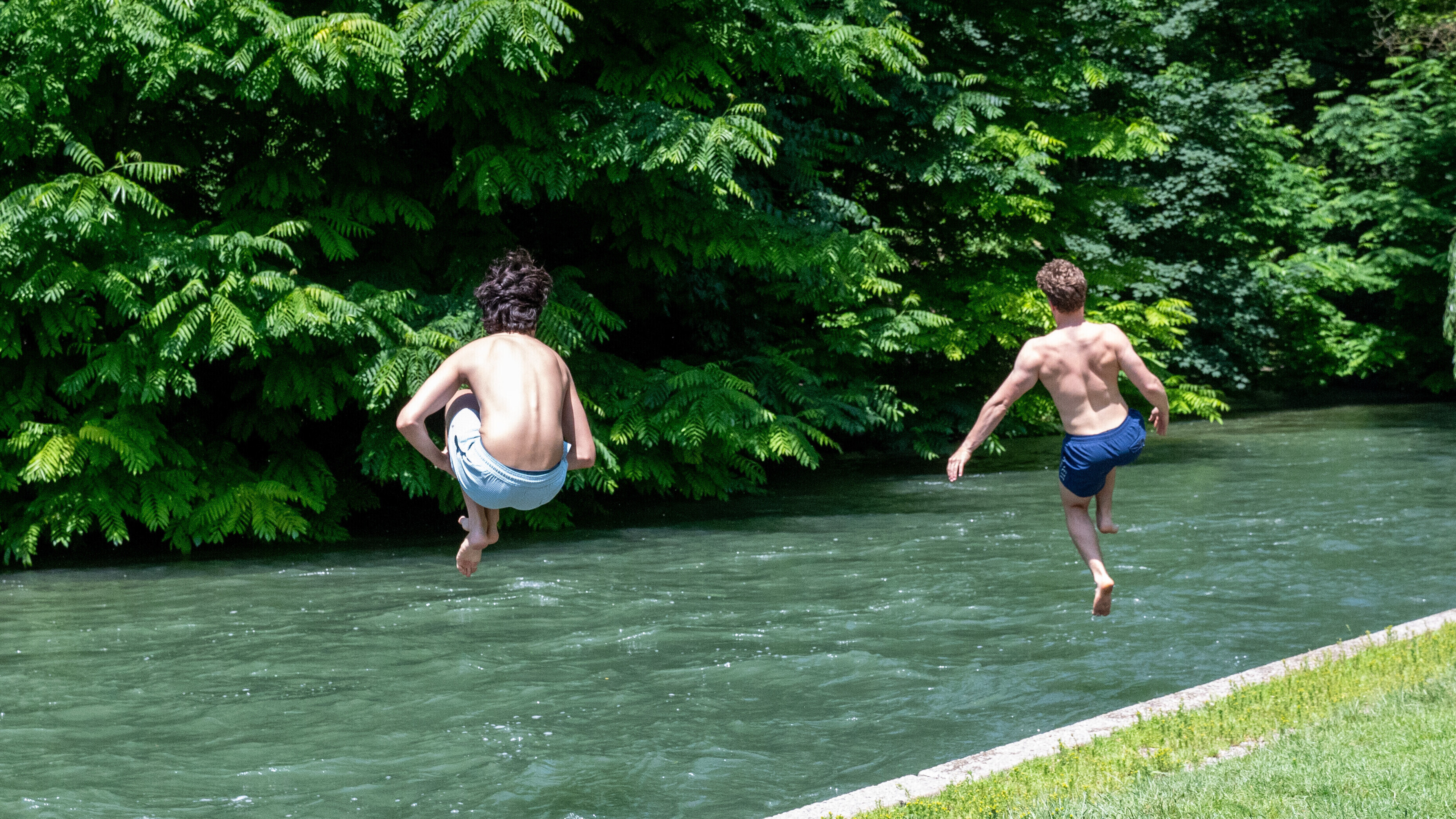 Zwei junge Männer springen zur Abkühlung in einen Bach