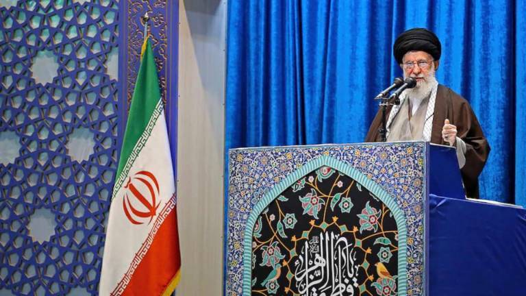Ayatalloh Ali Khamenei bei Rede vor blauem Samthintergrund neben iranischer Flagge