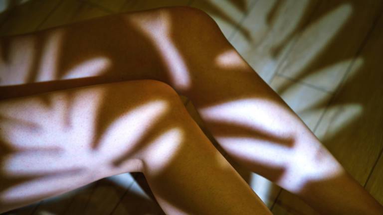 Beine einer Frau, auf denen Schatten von Blättern zu sehen sind