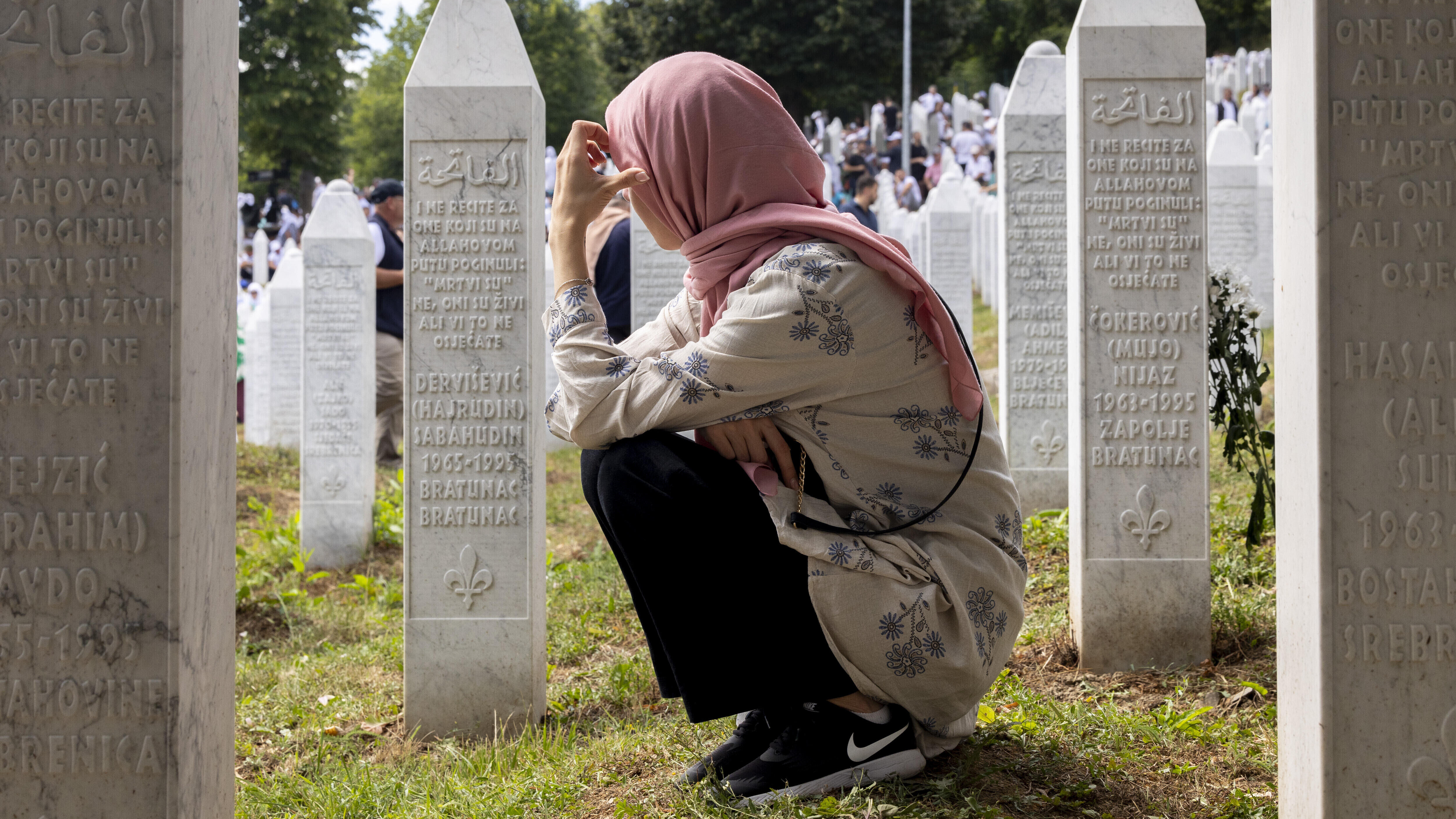 Eine Frau kniet am Mahnmal von Srebrenica