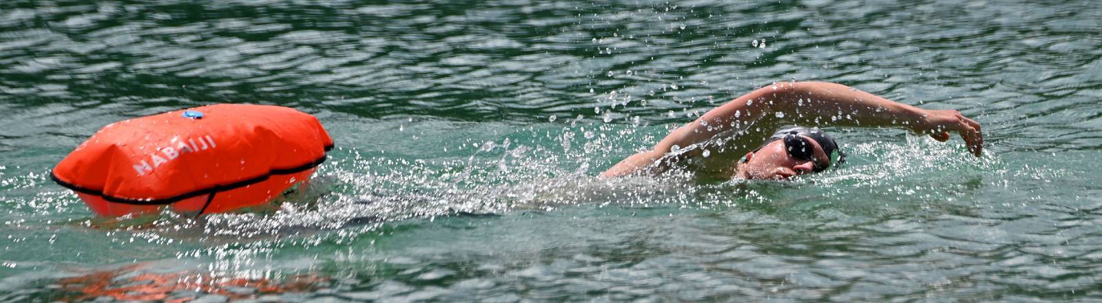 Ein Mann schwimmt im See. Er zieht eine Boje hinter sich her.