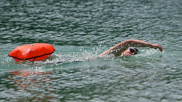 Ein Mann schwimmt im See. Er zieht eine Boje hinter sich her.