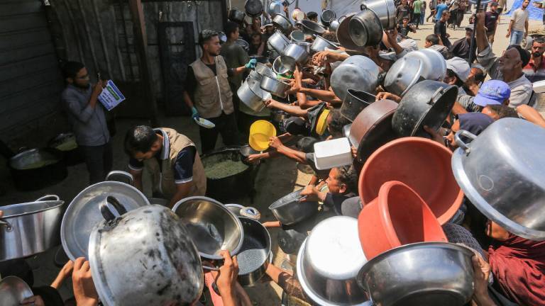 Palästinenser, darunter auch Kinder, die aufgrund der Blockade Israels und der anhaltenden Angriffe auf den Gazastreifen Schwierigkeiten haben, sich mit Lebensmitteln zu versorgen, stehen am 21. August 2025 in Khan Yunis im Gazastreifen in der Region Al-Mawasi Schlange, um warme Mahlzeiten zu erhalten, die von einer Wohltätigkeitsorganisation verteilt werden. Sie halten Töpfe und Schüsseln hoch über ihre Köpfe.