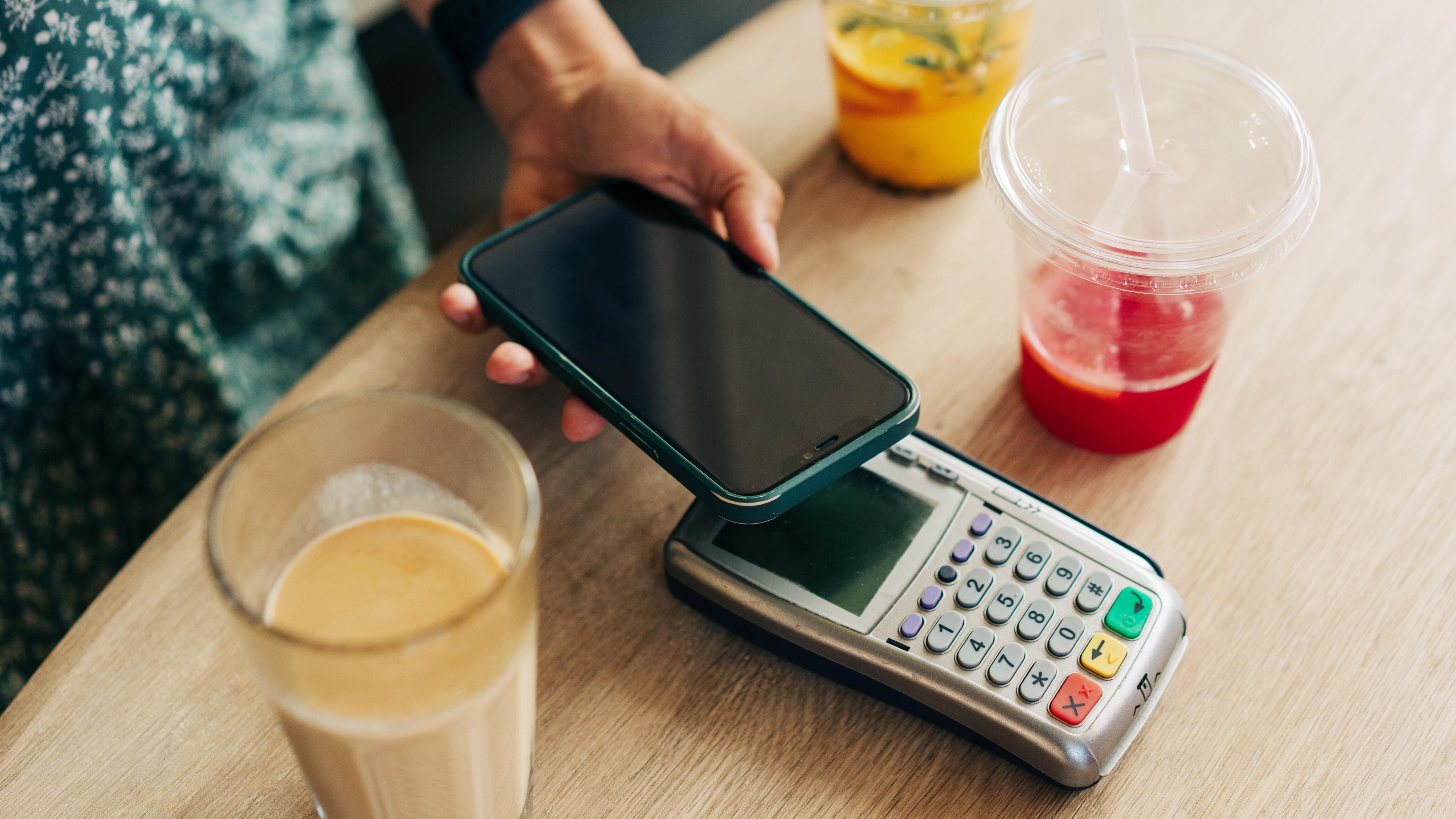 Nahaufnahme des kontaktlosen Bezahlens mit dem Mobiltelefon durch eine nicht erkennbare Person in einem Café.