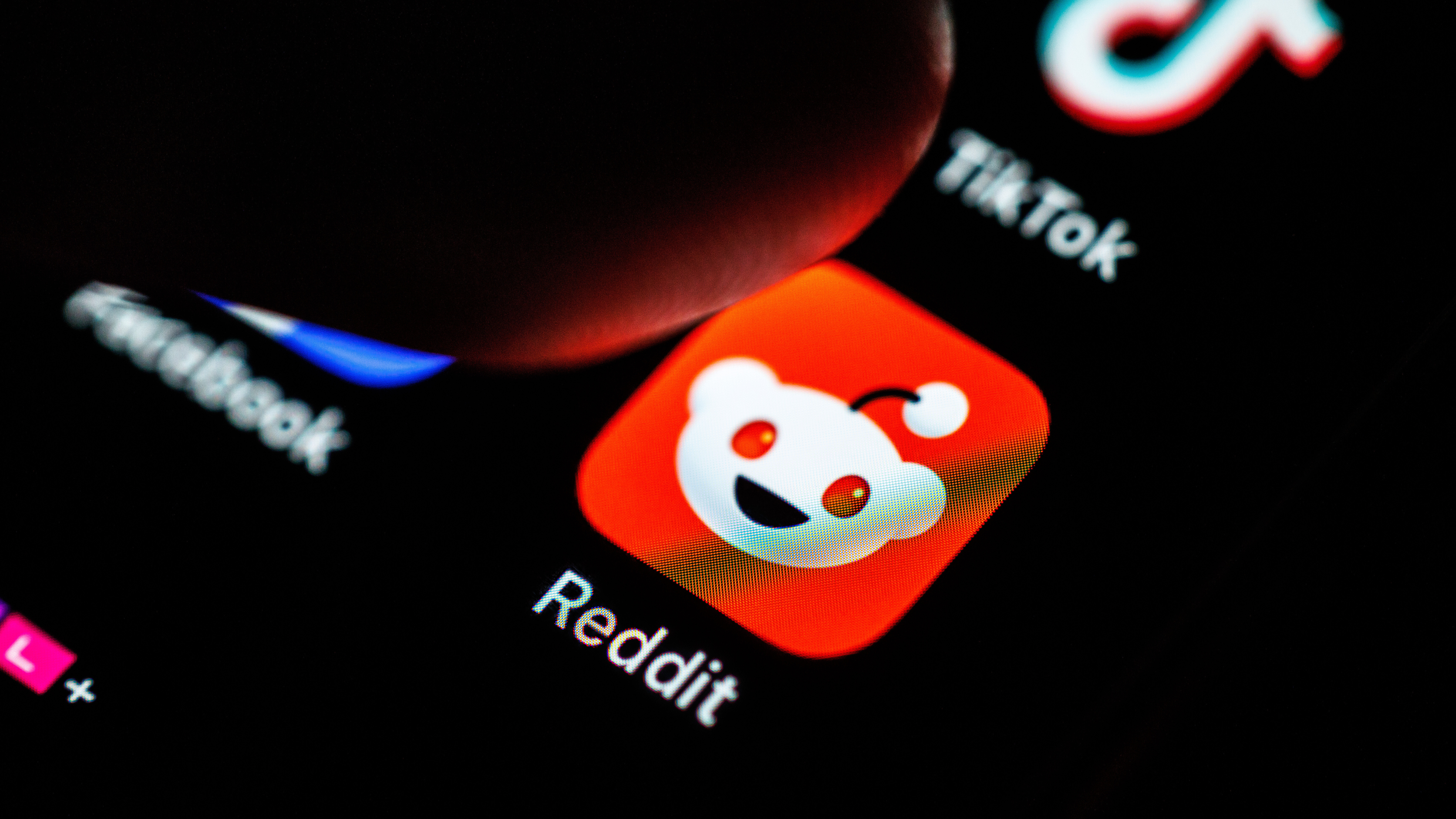 Ein Finger tippt auf einem Smartphone auf das Logo der Internetplattform Reddit.
