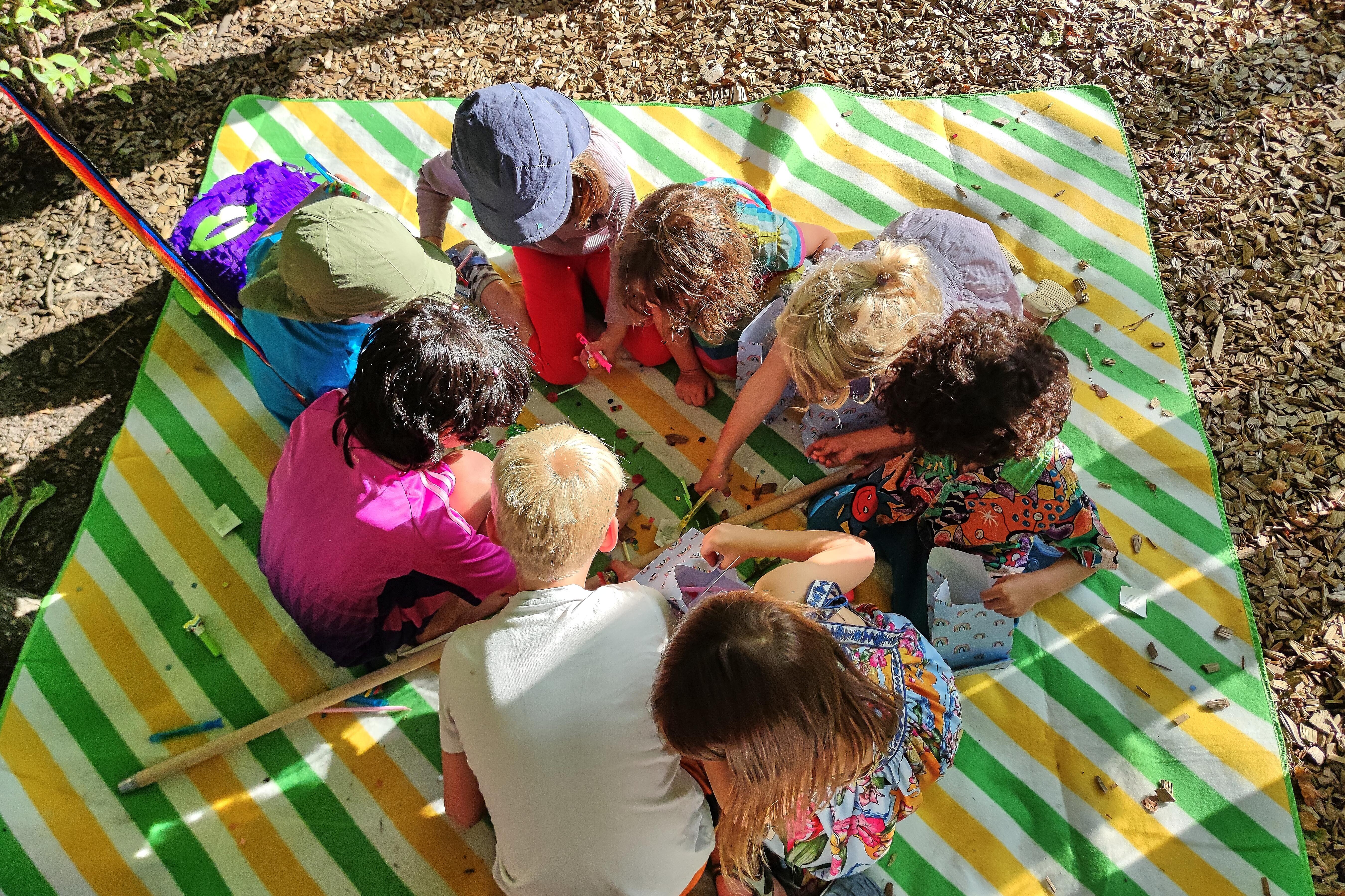 Berlin, Deutschland: Kinder sitzen bei einer Geburtstagsfeier auf einer Decke und beschäftigen sich mit Süßigkeiten