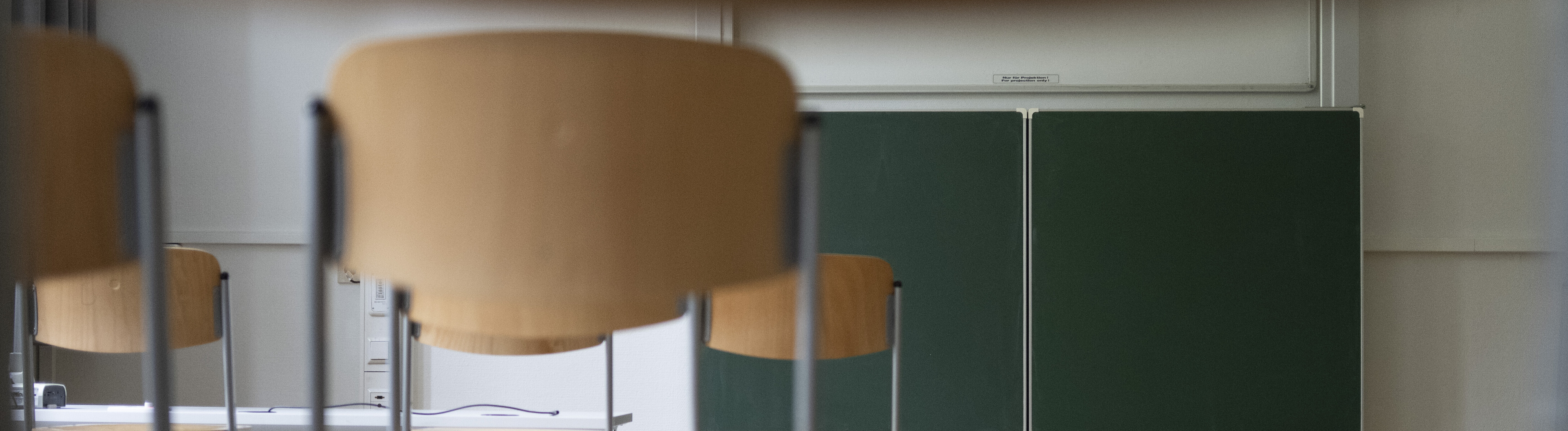 Stühle stehen auf Tischen in einem Klassenraum mit grüner Tafel im Hintergrund