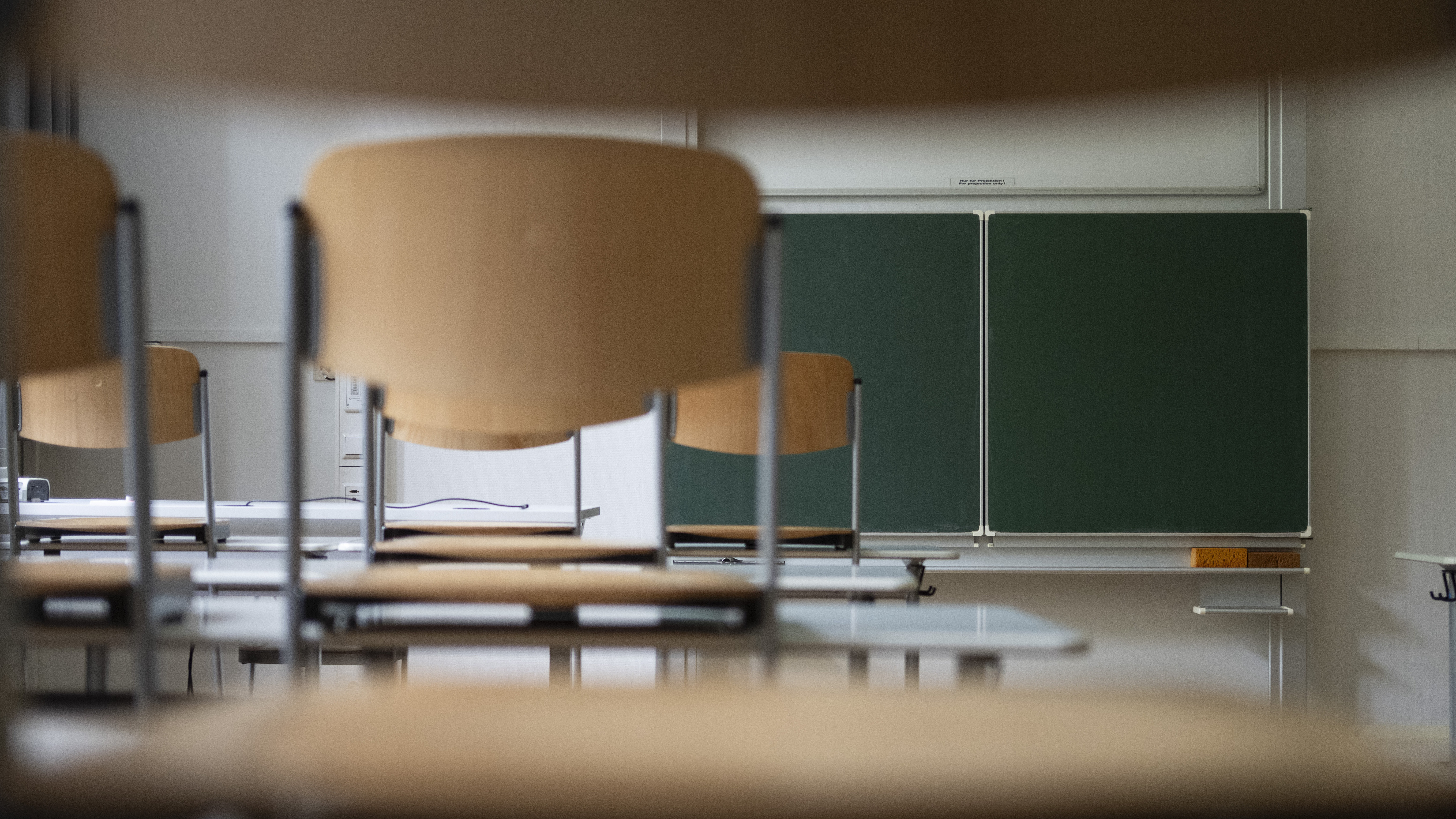 Stühle stehen auf Tischen in einem Klassenraum mit grüner Tafel im Hintergrund