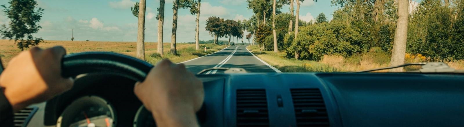 Ein Person sitzt am Steuer eines Autos und fährt eine Landstraße entlang