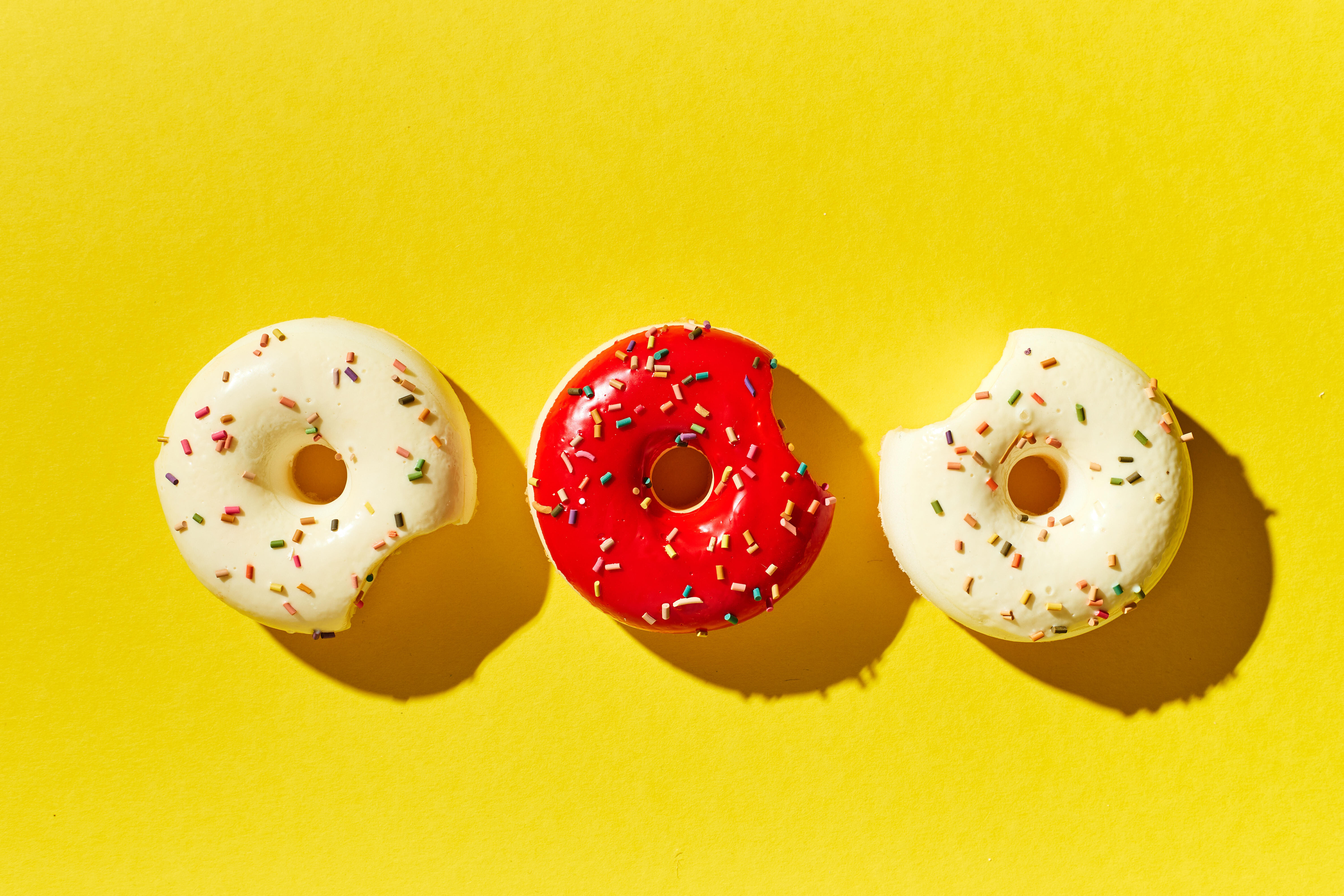 Drei Donuts, zwei in weiß und einer in rot, auf gelbem Hintergrund
