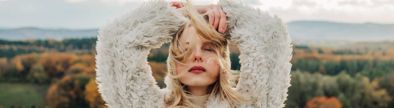 Frau mit geschlossenen Augen und Armen und dem Kopf geschlagen steht vor Naturpanorama