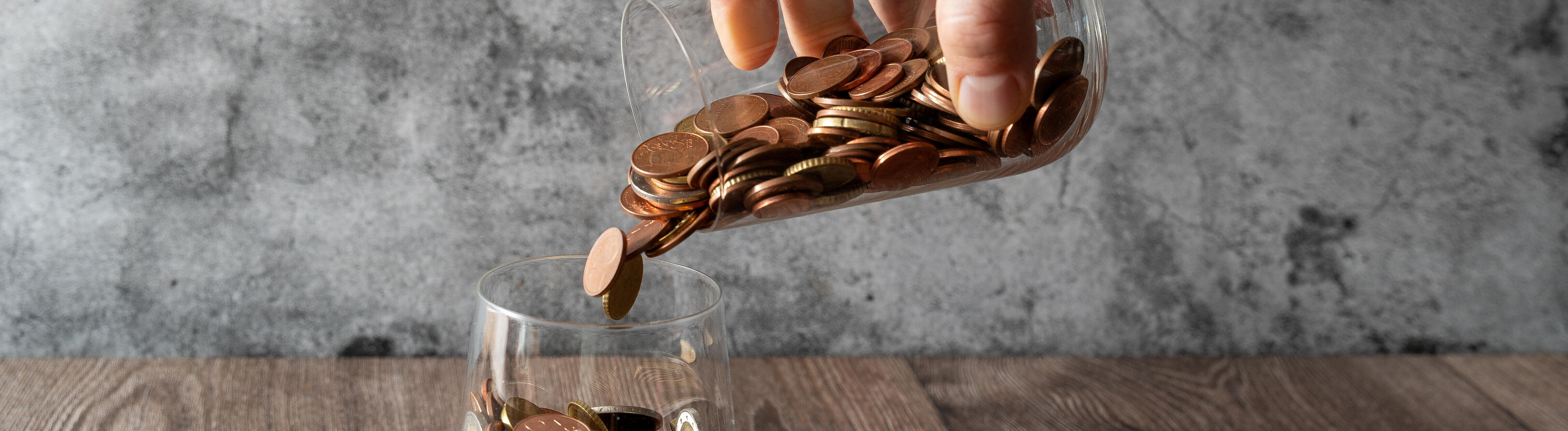 Hand schüttet Münzen aus einem Glas in ein anderes