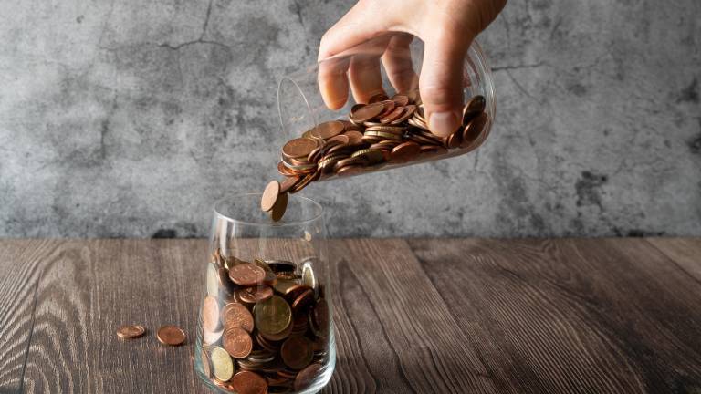 Hand schüttet Münzen aus einem Glas in ein anderes