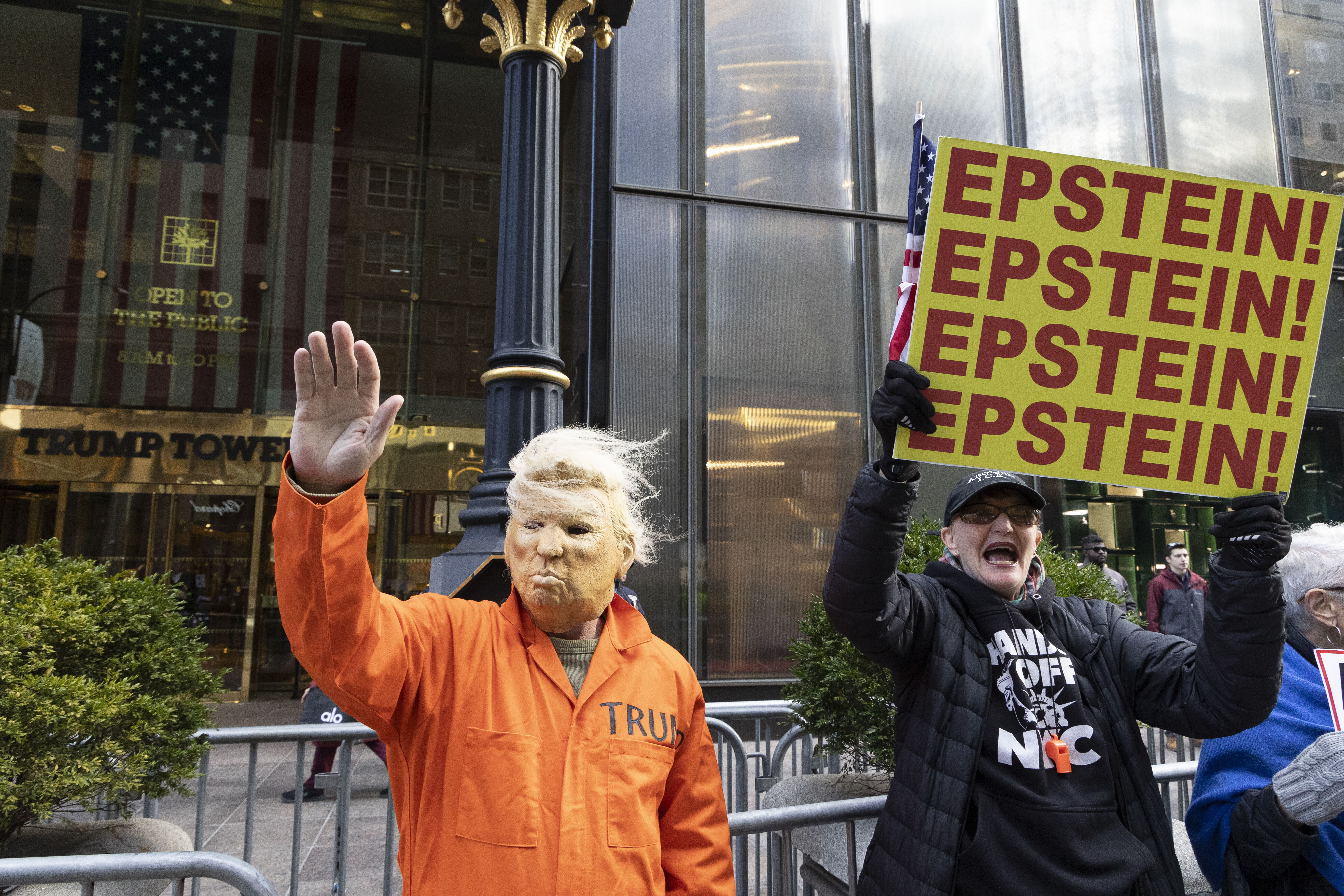 16. November 2025, New York, New York, USA: Ein Mann mit einer Trump-Maske und einem orangefarbenen Gefängnisoverall winkt Passanten auf der Fifth Avenue zu und schließt sich friedlichen Anti-Trump-Demonstranten vor dem Trump Tower an, die Schilder mit der Aufschrift „EPSTEIN! EPSTEIN! EPSTEIN! EPSTEIN!” hochhalten.