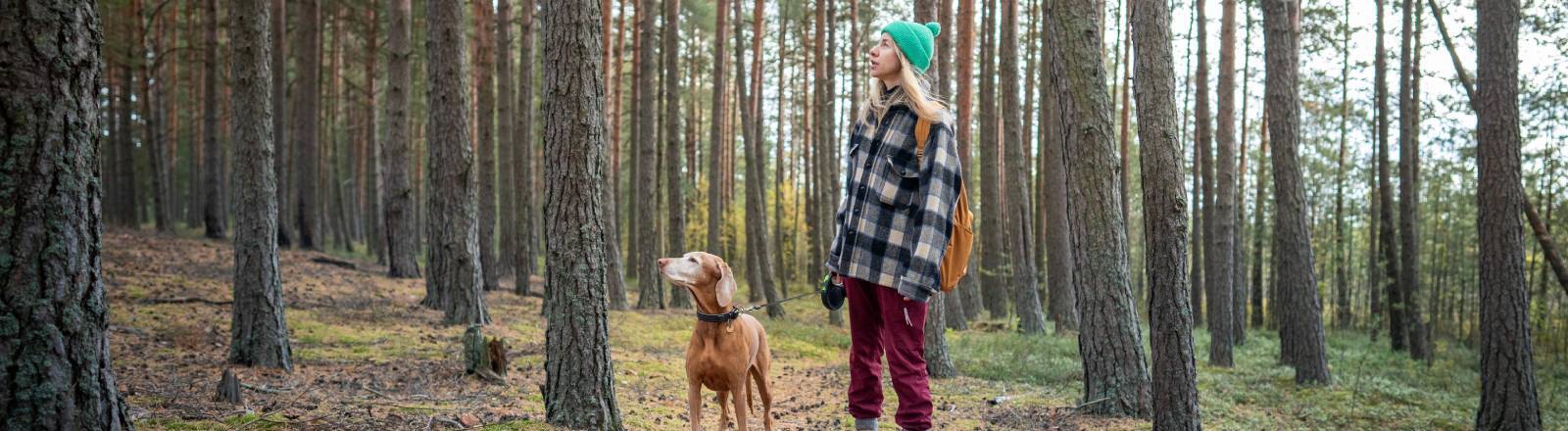 Eine Frau steht mit einem Hund im Wald