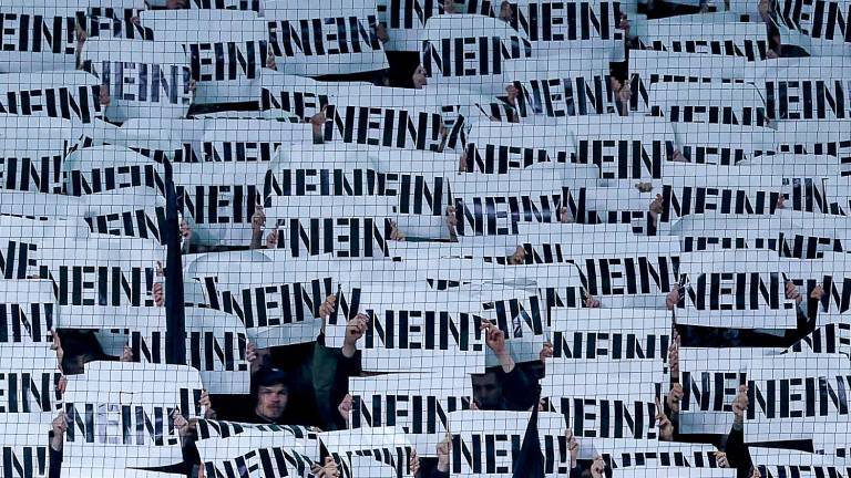 Fußballfans halten Schilder als Protest gegen die Pläne des Bundesinnenministers mit der Aufschrift „NEIN“ vor ihre Gesichter (Borussia-Park Mönchengladbach, 28.11.2025)