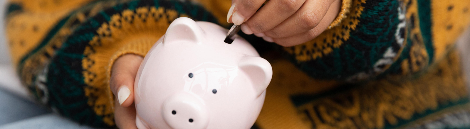 Eine Hand wirft eine Münze in ein Sparschwein