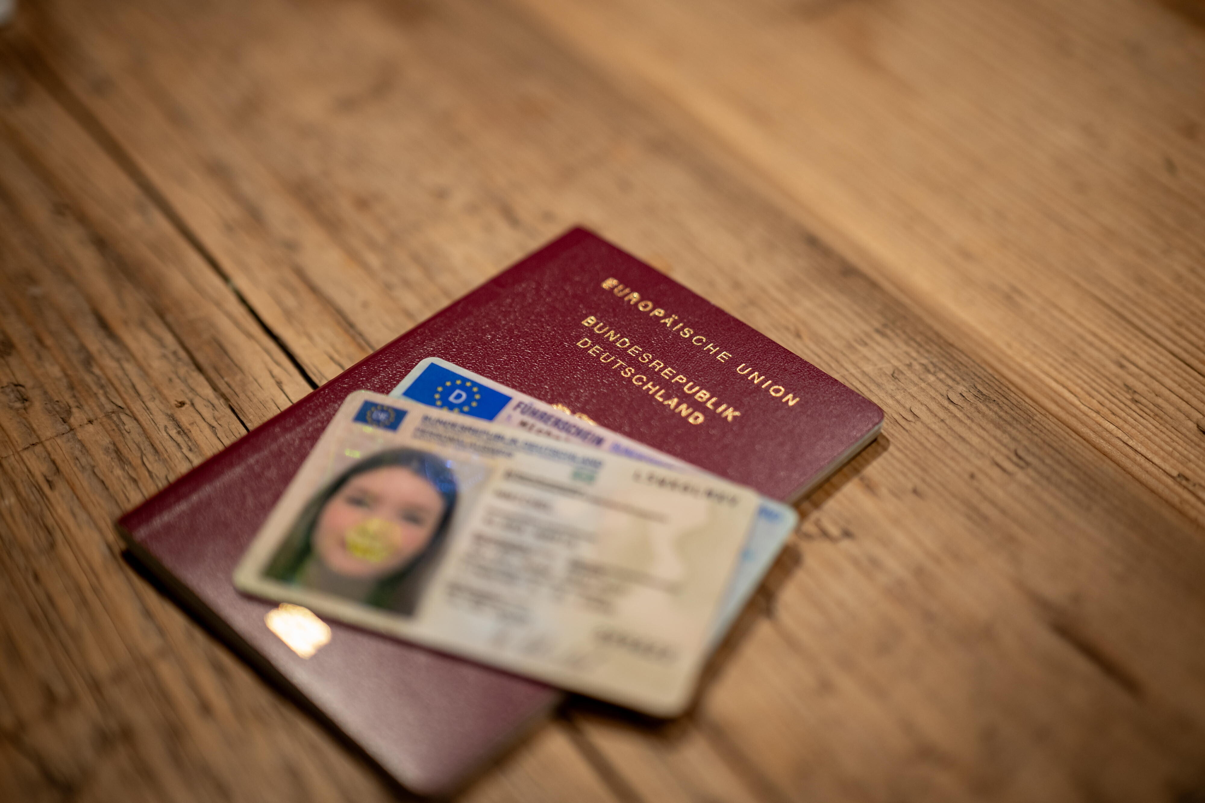 Eine Hand hält einen deutschen Reisepass zusammen mit einem Führerschein über einem Holztisch.