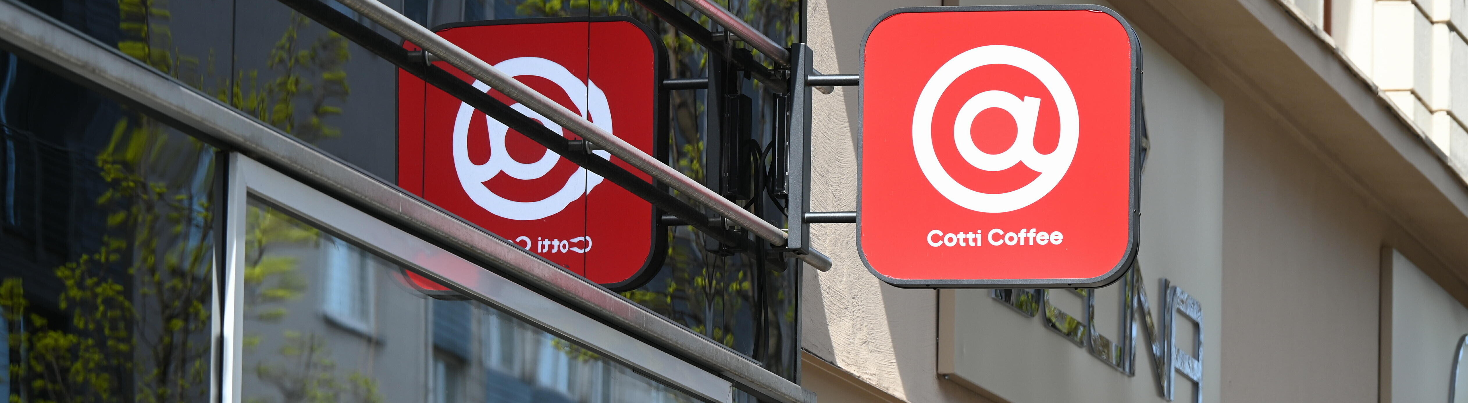 Schild der Kaffeekette Cotti Coffee an einer Hausfassade - ein weißes @-Zeichen auf rotem Grund