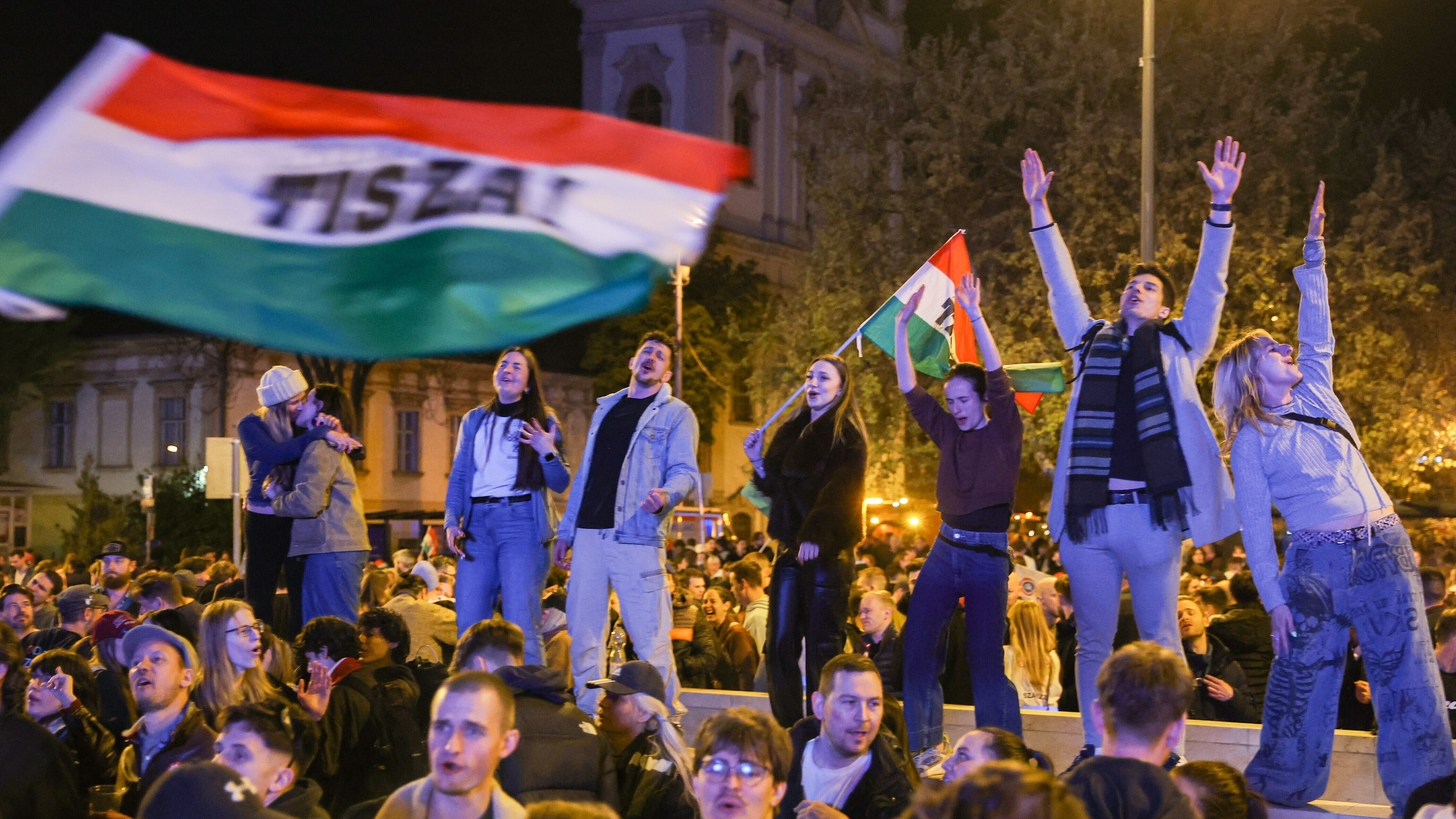 Junge Leute stehen auf einer Mauer und schwenken Ungarn-Flaggen nach dem Wahlsieg von  Péter Magyar (Budapest 13.04.2026)