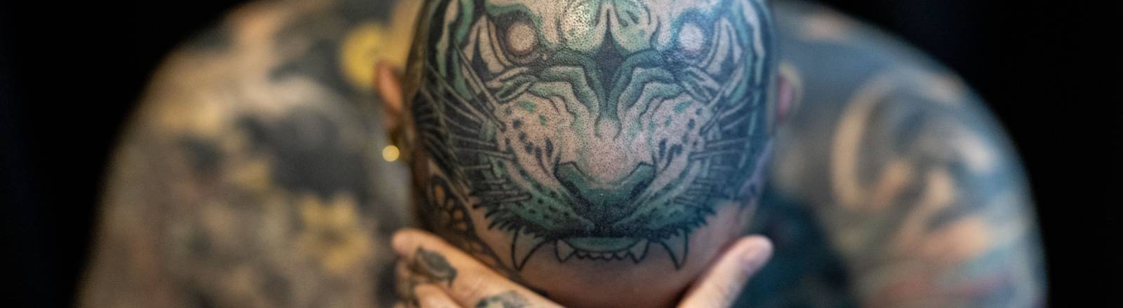 Ein Mann zeigt seine Tattoos, wobei der Kopf mit dem Bild eines Tigers verziert ist