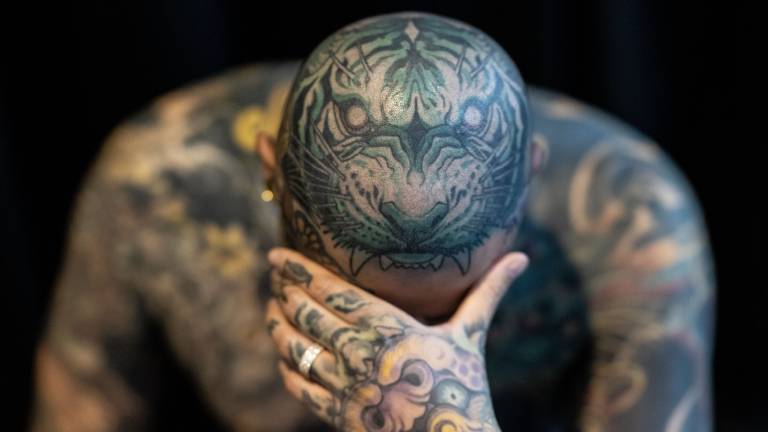 Ein Mann zeigt seine Tattoos, wobei der Kopf mit dem Bild eines Tigers verziert ist