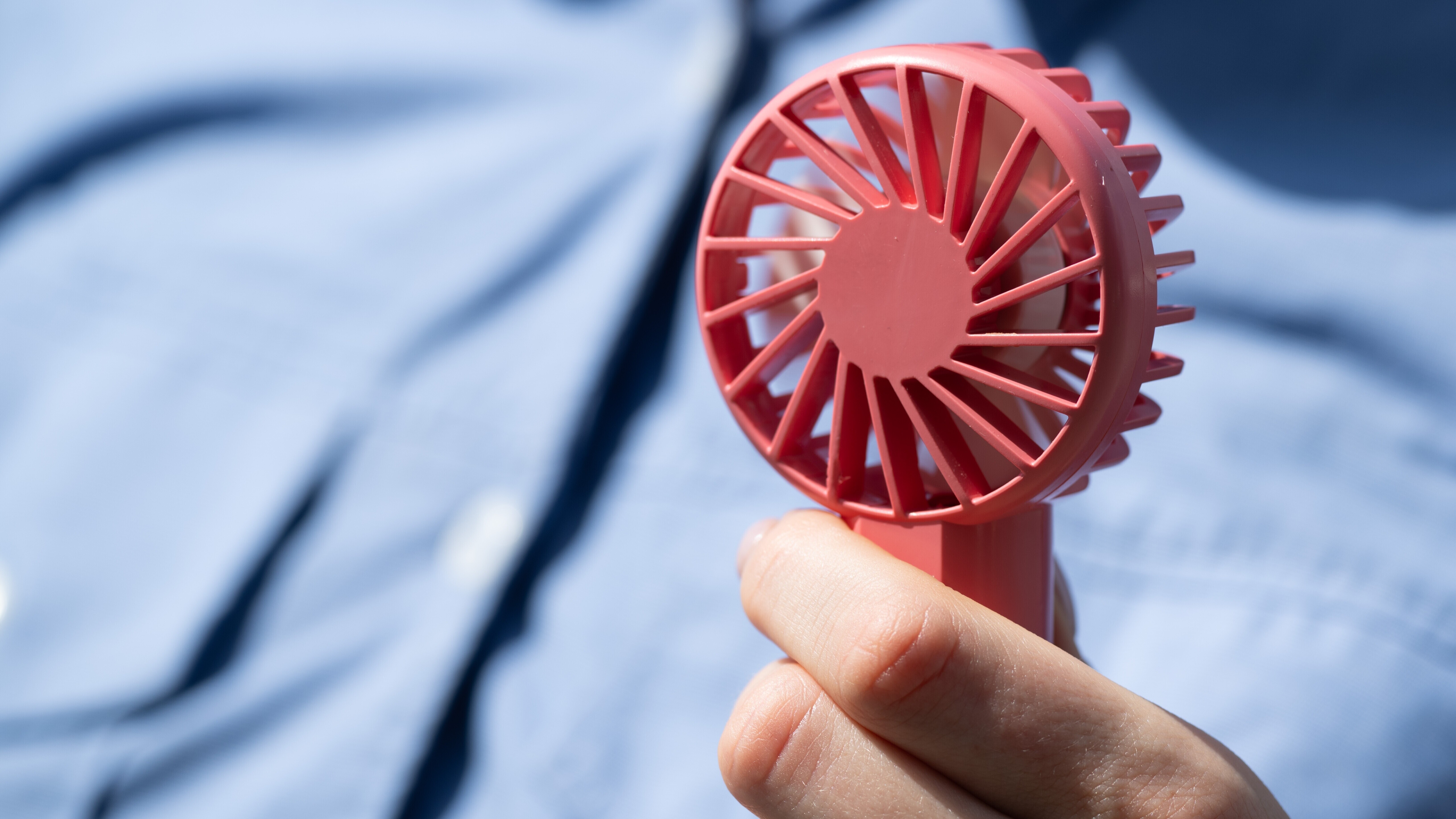 Ein kleiner rosafarbener Handventilator vor einem blauen Hemd
