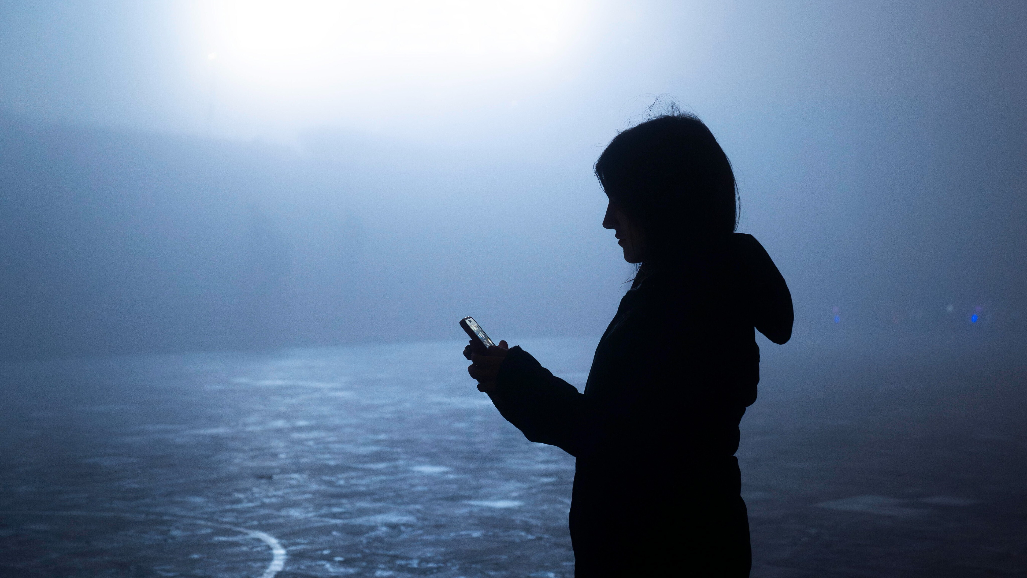 Silhouette einer Person, die im Halbdunkel auf ein Smartphone schaut.