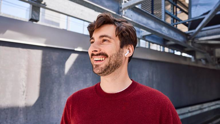 Ein single-Mann trägt Ear-Pods, roten Pulli und genießt den sonnigen Tag an der frischen Luft.