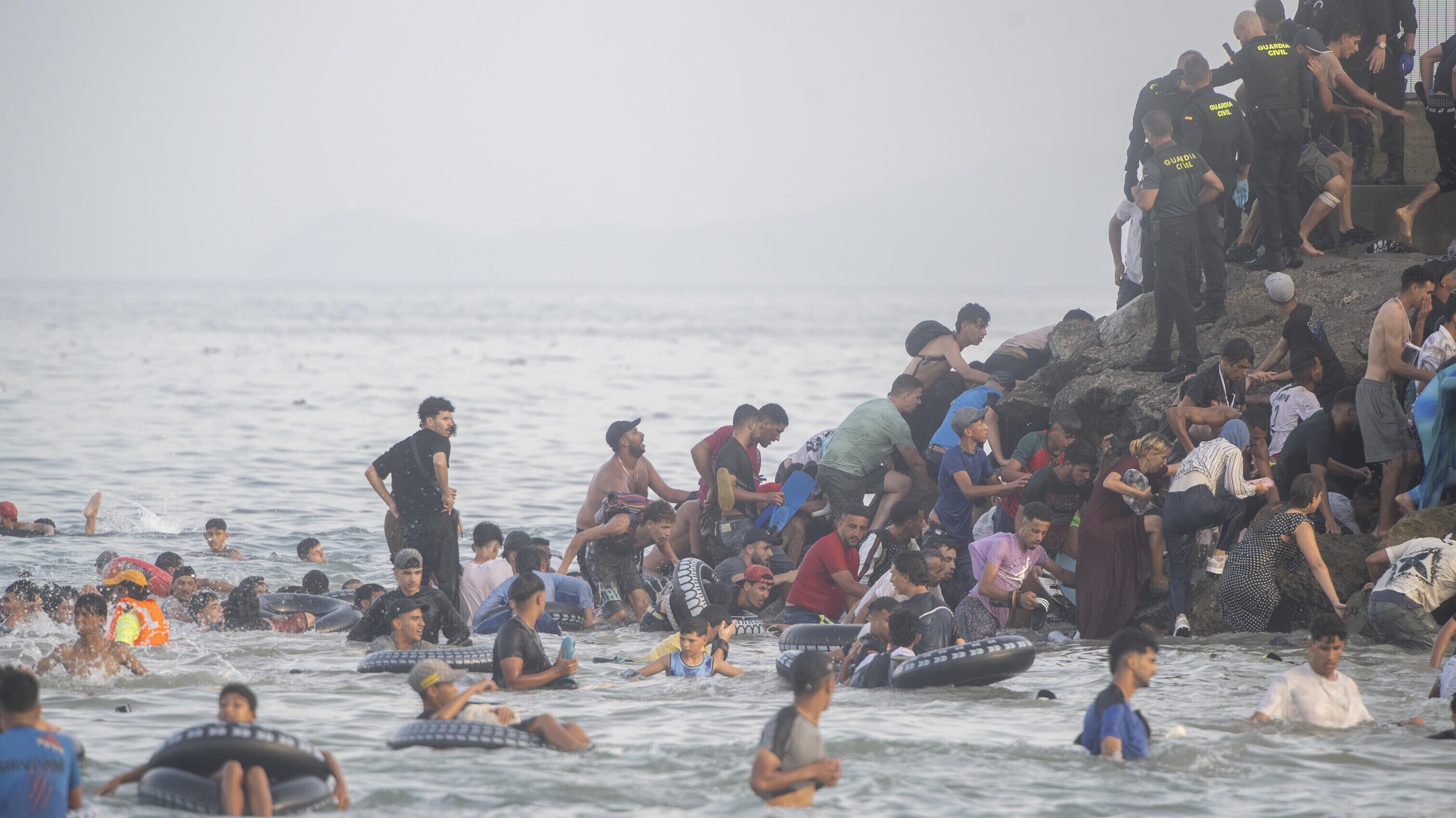 Menschen schwimmen im Meer und klettern auf einen Felsen, auch Sicherheitskräfte sind vor Ort