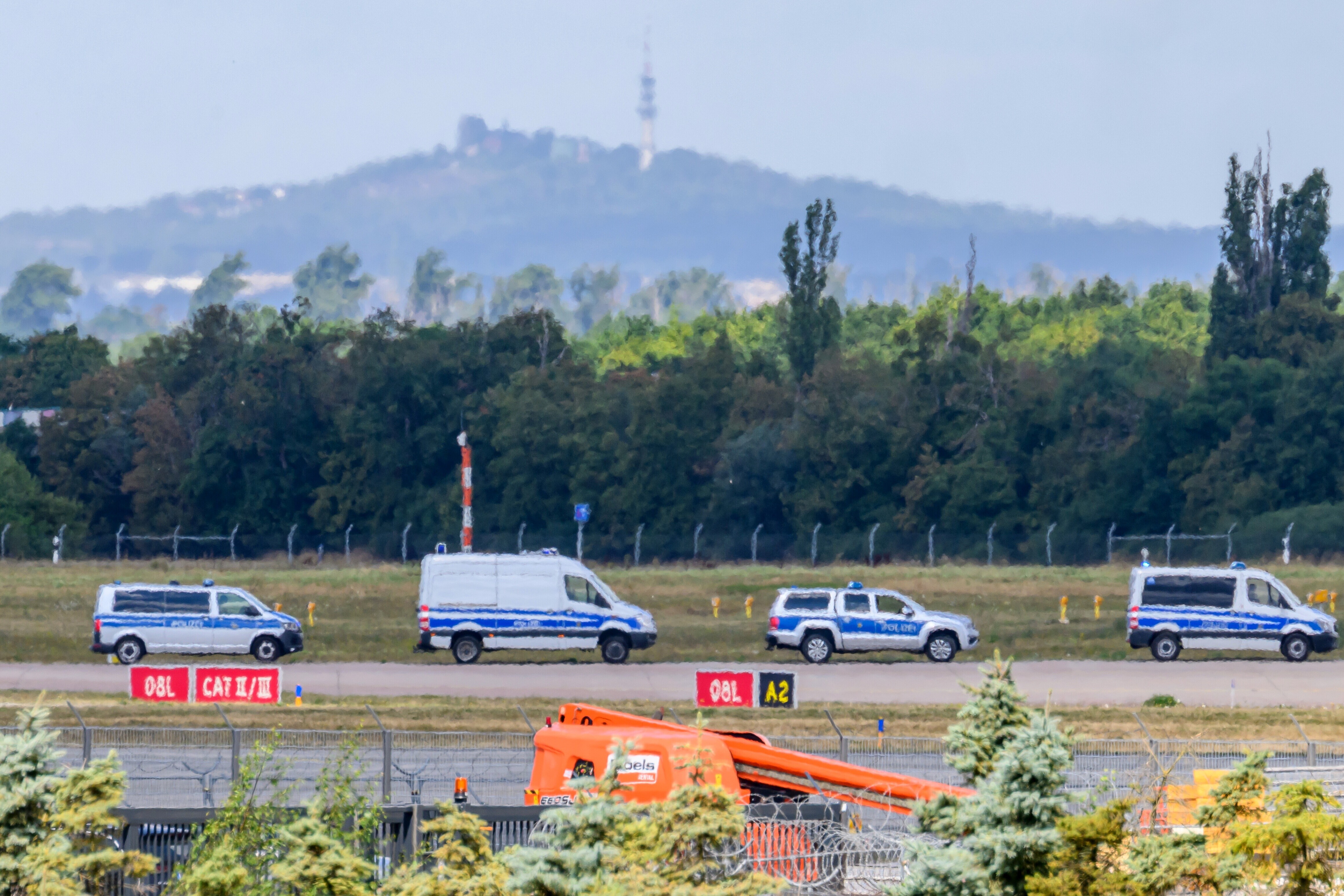 Vor der Silhouette des Petersberges fahren Einsatzkräfte der Polizei entlang der Start-und-Lande-Bahn Nord des Flughafens Leipzig/Halle.