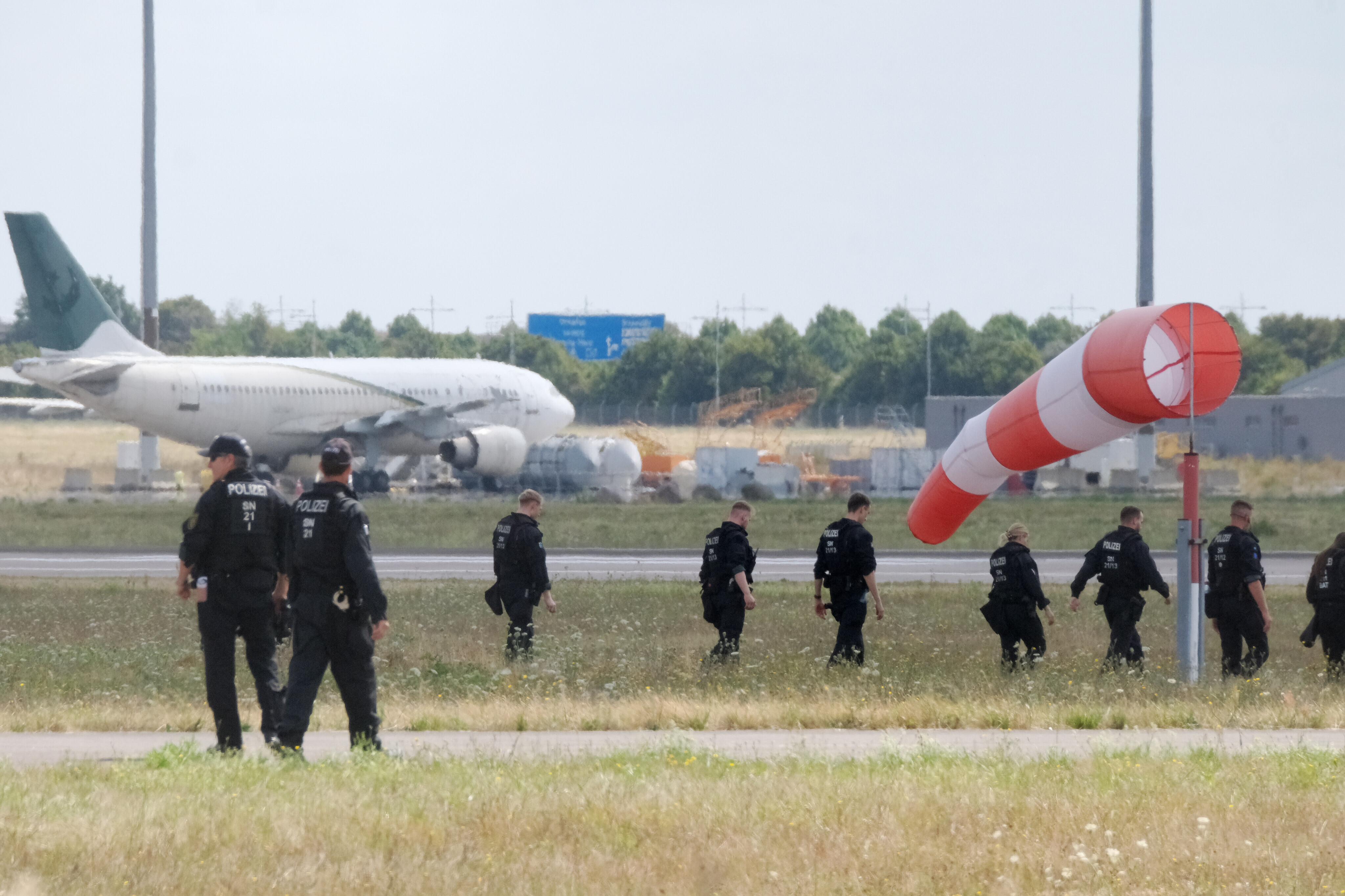 Polizisten gehen über eine Wiese auf dem Gelände des Flughafen Leipzig/Halle (7.08.2026)