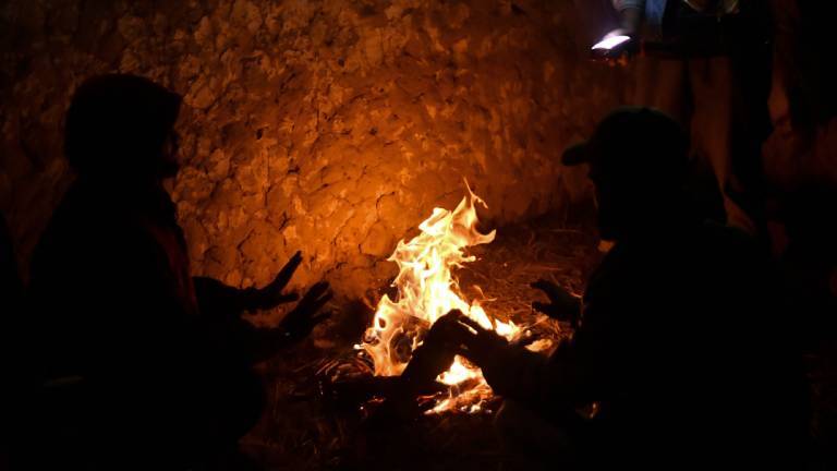 Menschen sitzen um ein Feuer verteilt und wärmen sich.