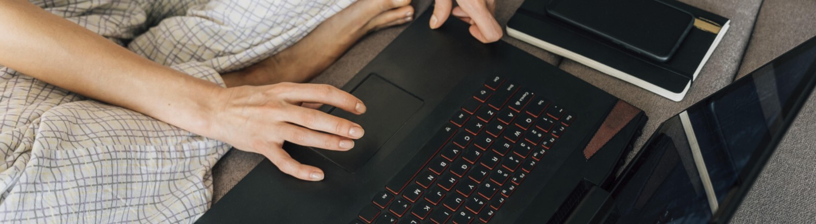 Eine Frau in Hauskleidung mit einem Laptop, neben ihr ein Notizbuch und ein Stift.