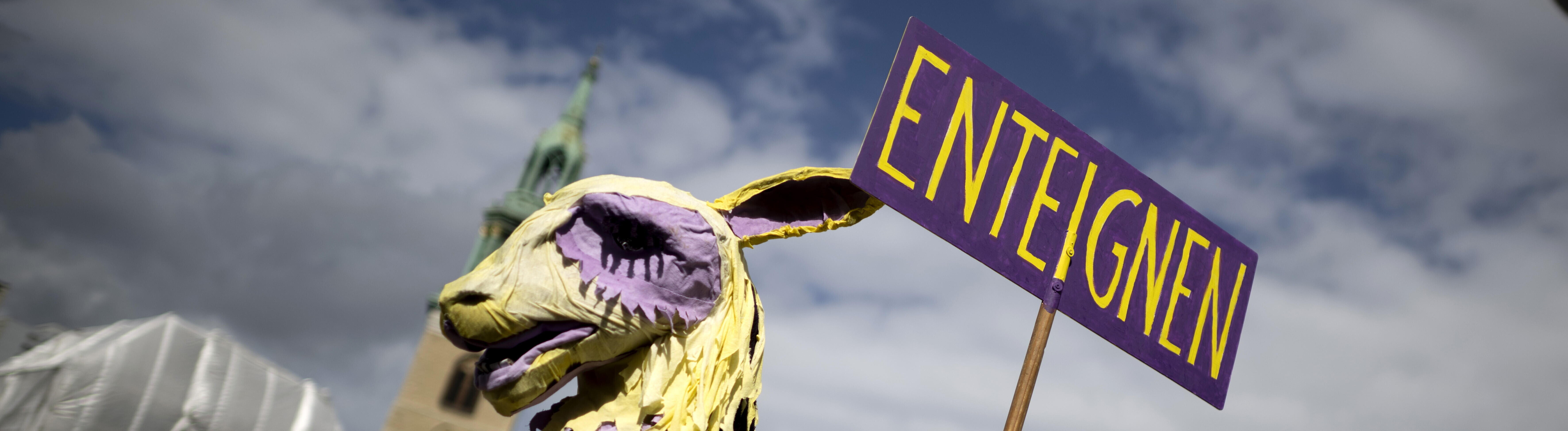 Demonstrant der Initiative Volksentscheid Deutsche Wohnen und Co ist als lila-gelbes Einhorn oder Trojanisches Pferd verkleidet und hält ein Schild mit dem Wort "Enteignung" in die Höhe (05.09.2026, Berlin)