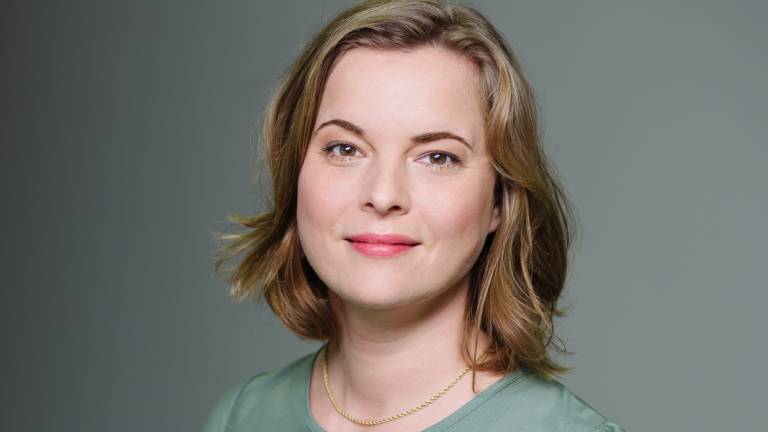 Portrait von Katja Berlin im olivegrünen Oberteil vor grauer Wand.