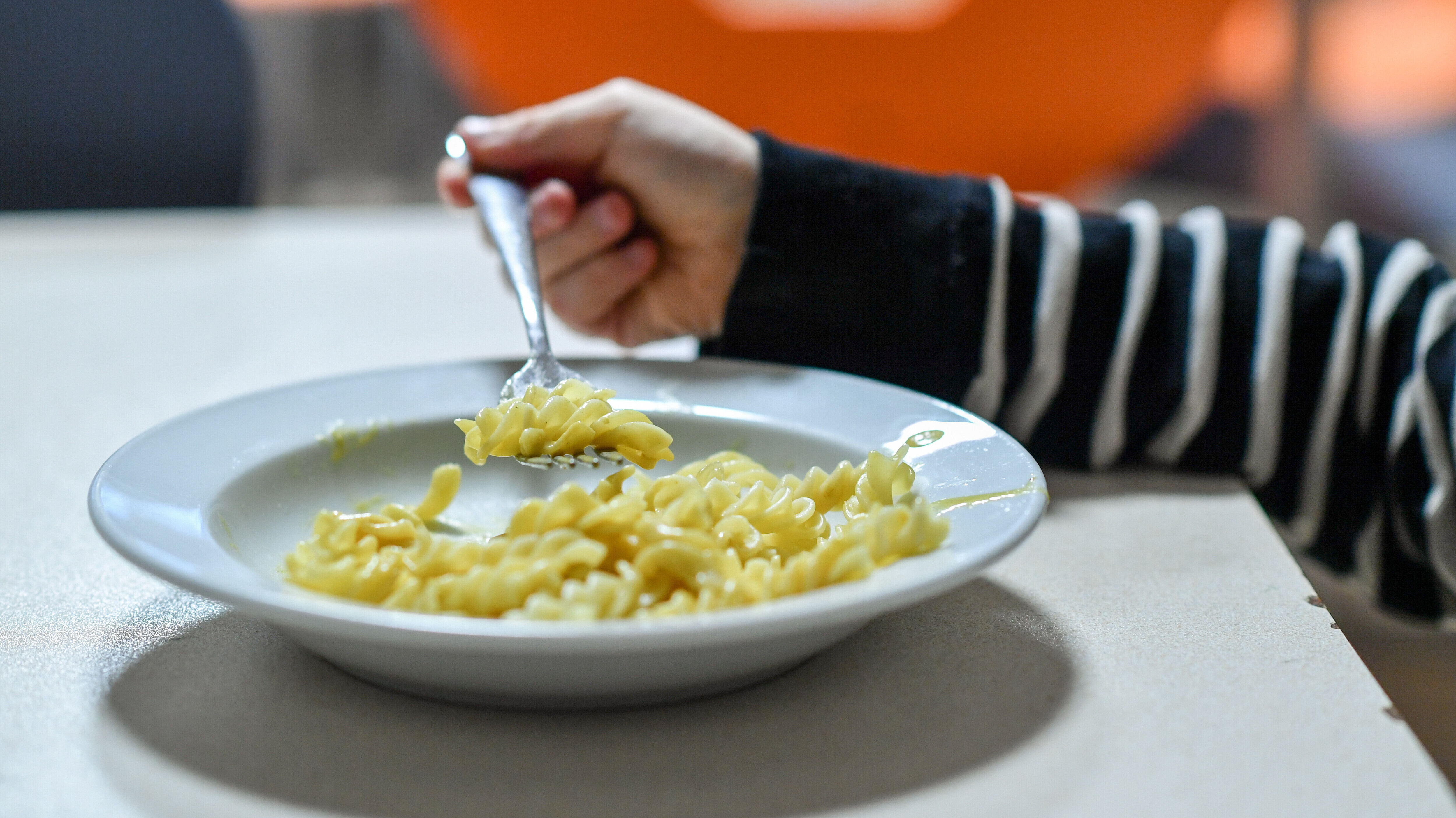 Ein Kind isst Nudeln von einem Teller.