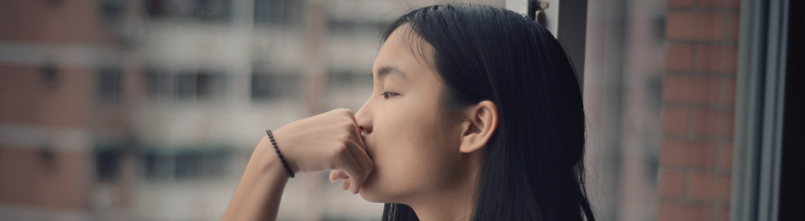 Eine junge Frau schaut grübelnd aus dem Fenster.