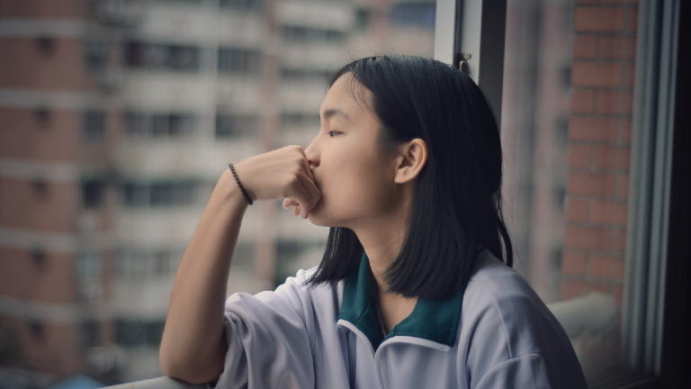 Eine junge Frau schaut grübelnd aus dem Fenster.