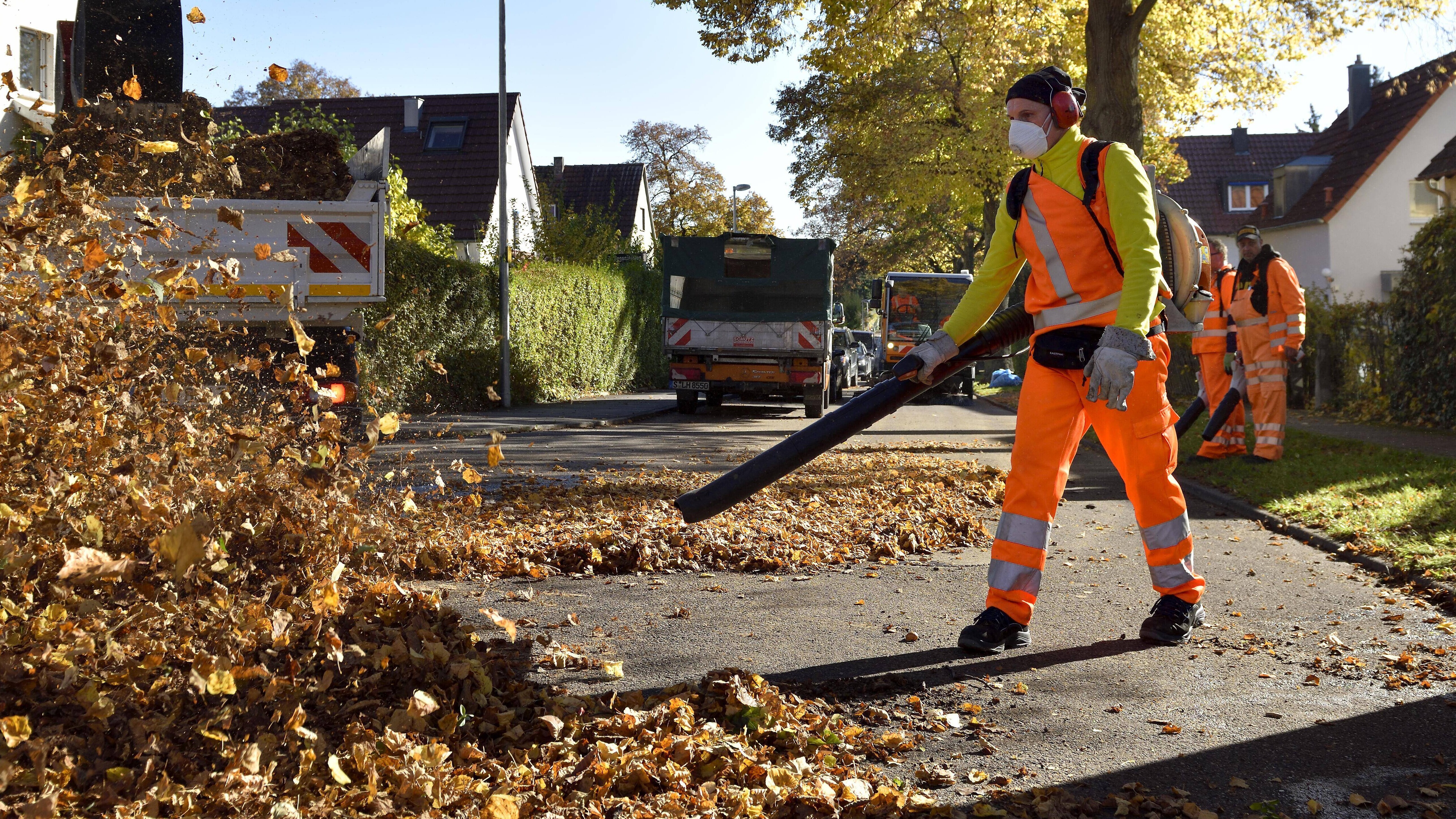 Ein Mitarbeiter der Straßenreinigung pustet mit einem Laubbläser das Laub weg.