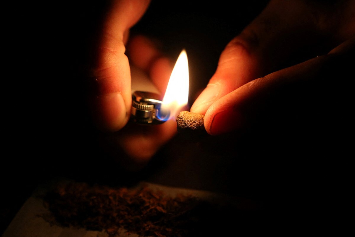 Zwei Hände im Dunkeln: Die eine Hand hält ein Stück Marihuana, die andere ein Feuerzeug mit Flamme.